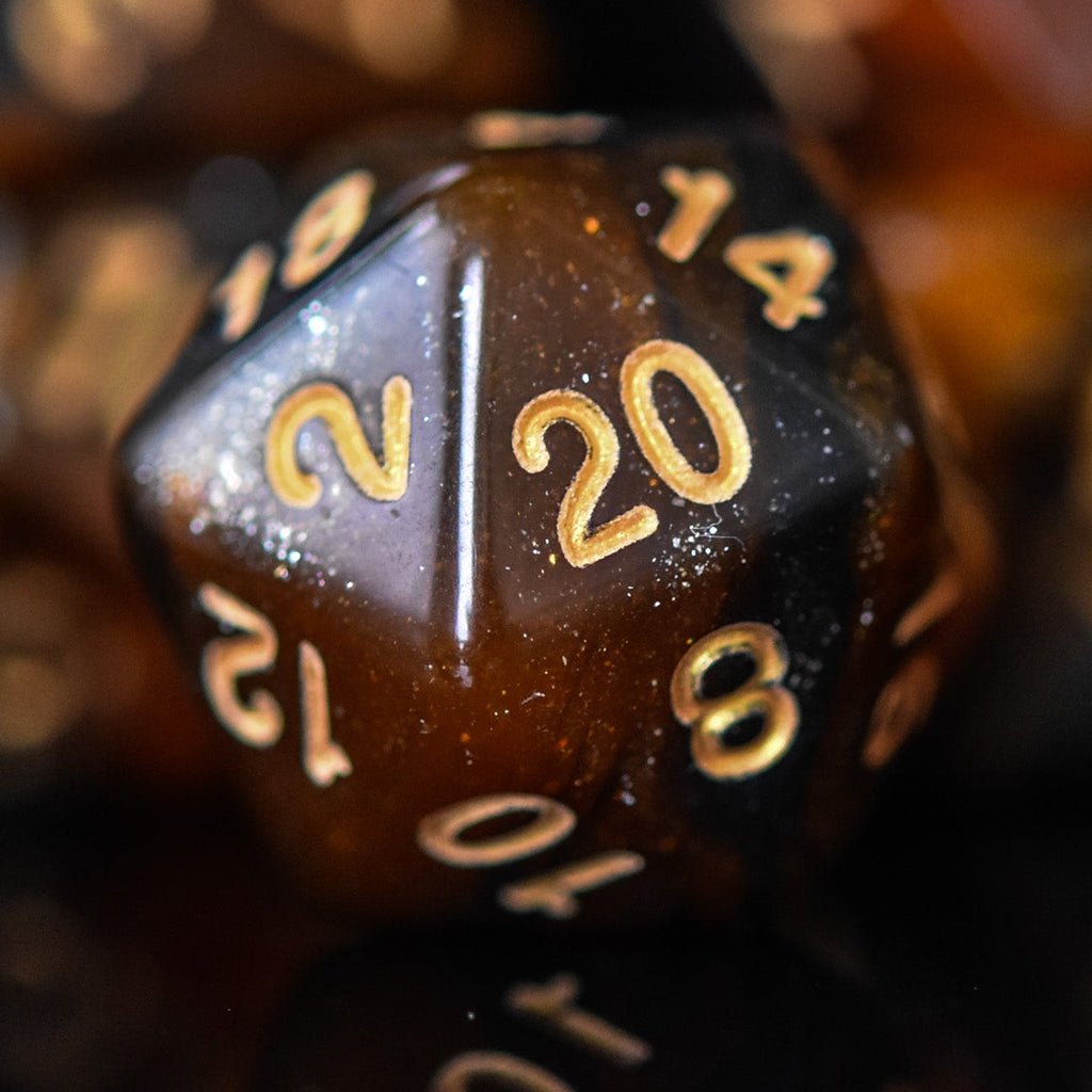 A set of acrylic dice with engraved numbers, featuring a brown color with gold accents, displayed on a reflective surface.