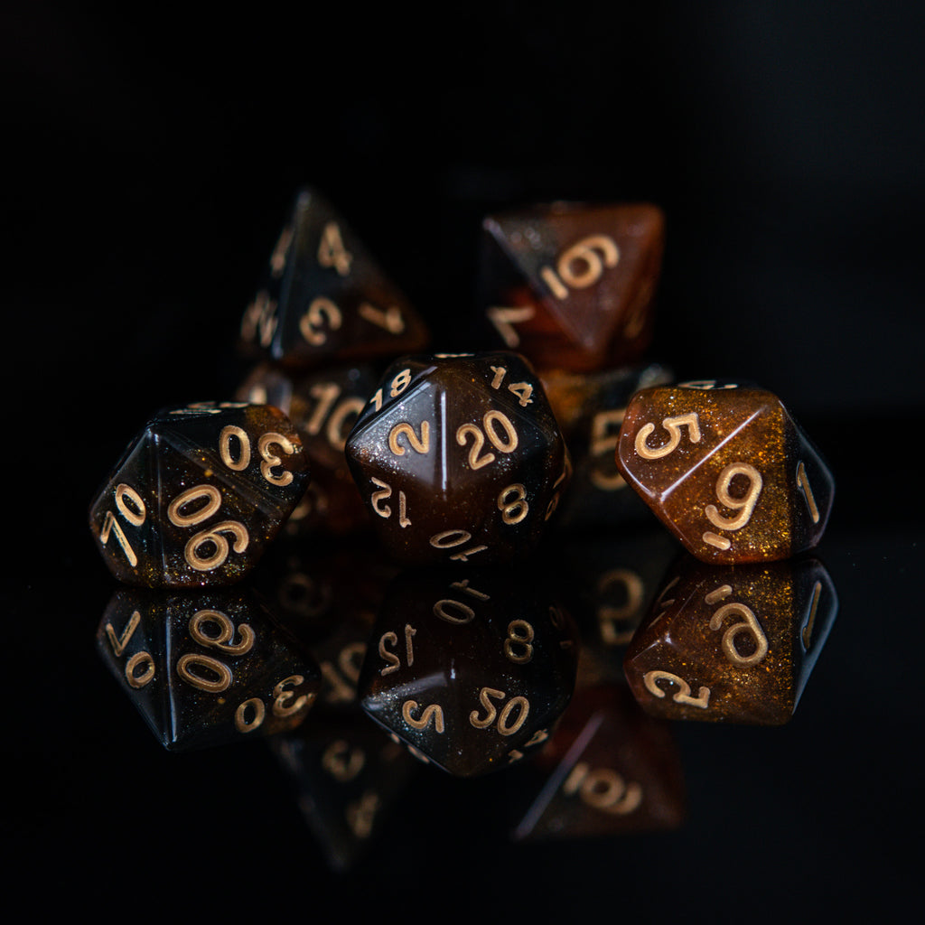 A set of acrylic dice with engraved numbers, featuring a brown color with gold accents, displayed on a reflective surface.