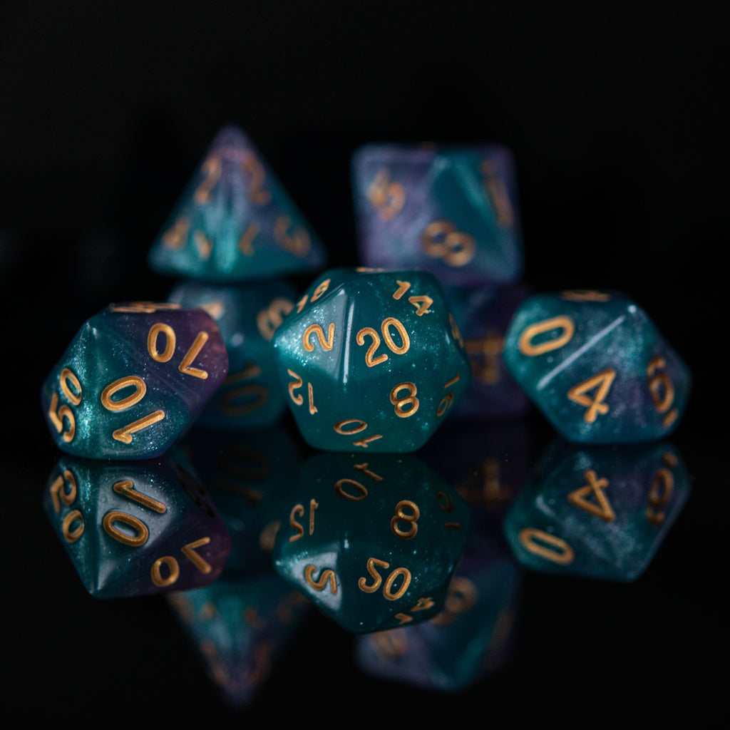 A set of acrylic ttrpg dice with engraved gold numbers, featuring a teal color with purple highlights, displayed on a reflective surface.