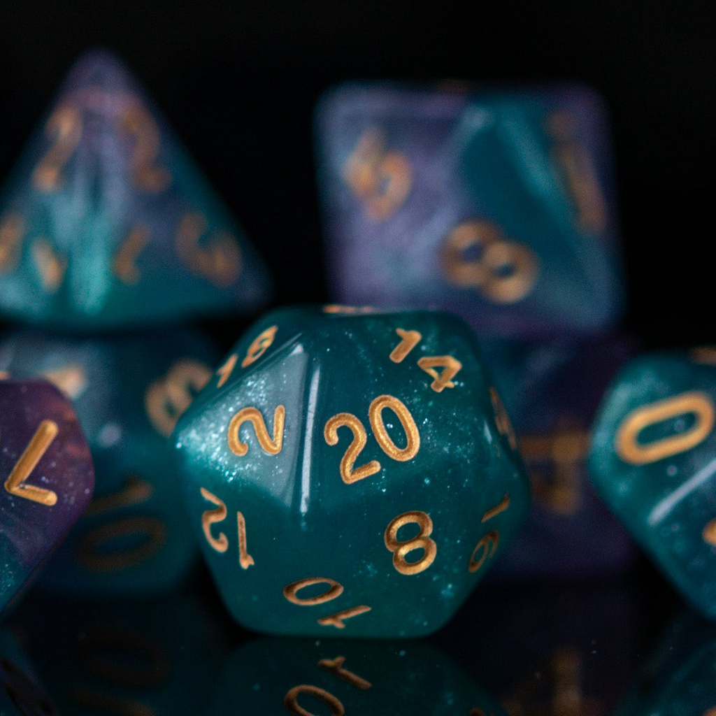 A set of acrylic ttrpg dice with engraved gold numbers, featuring a teal color with purple highlights, displayed on a reflective surface.