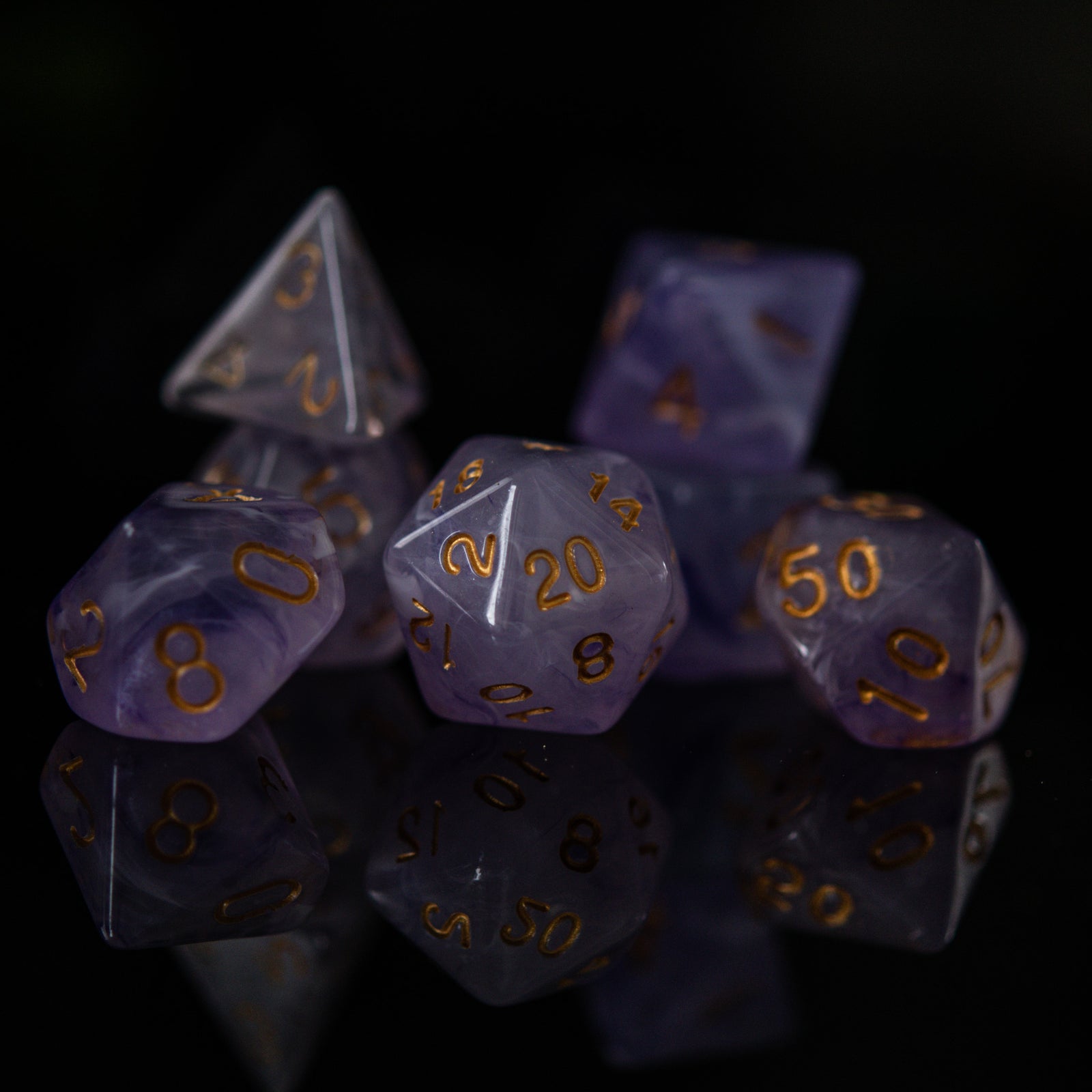 A set of creamy purple acrylic dice with golden engraved numbers, displayed on a reflective surface.