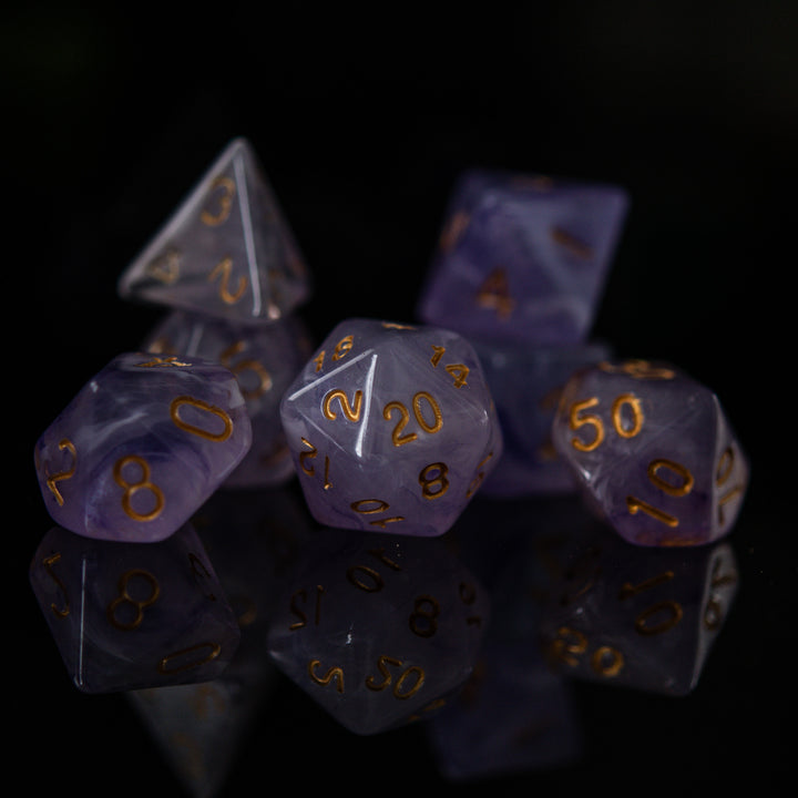 A set of creamy purple acrylic dice with golden engraved numbers, displayed on a reflective surface.