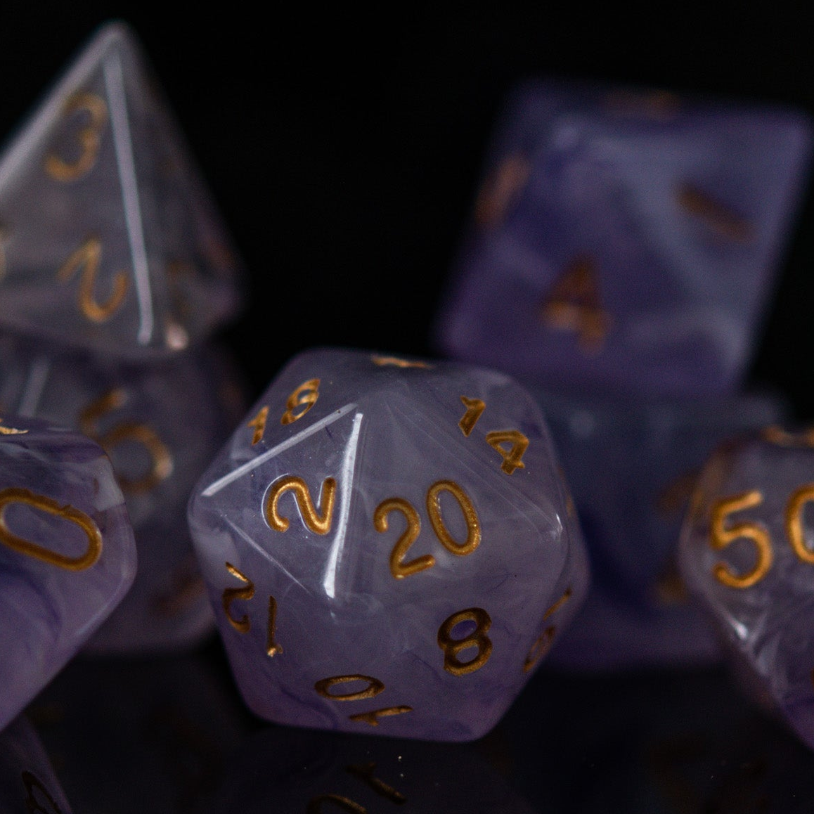 A set of creamy purple acrylic dice with golden engraved numbers, displayed on a reflective surface.