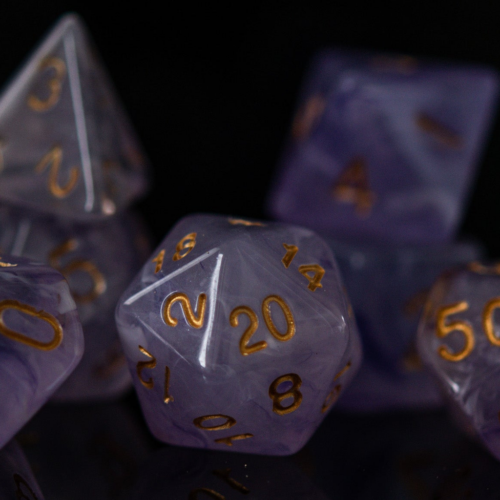 A set of creamy purple acrylic dice with golden engraved numbers, displayed on a reflective surface.