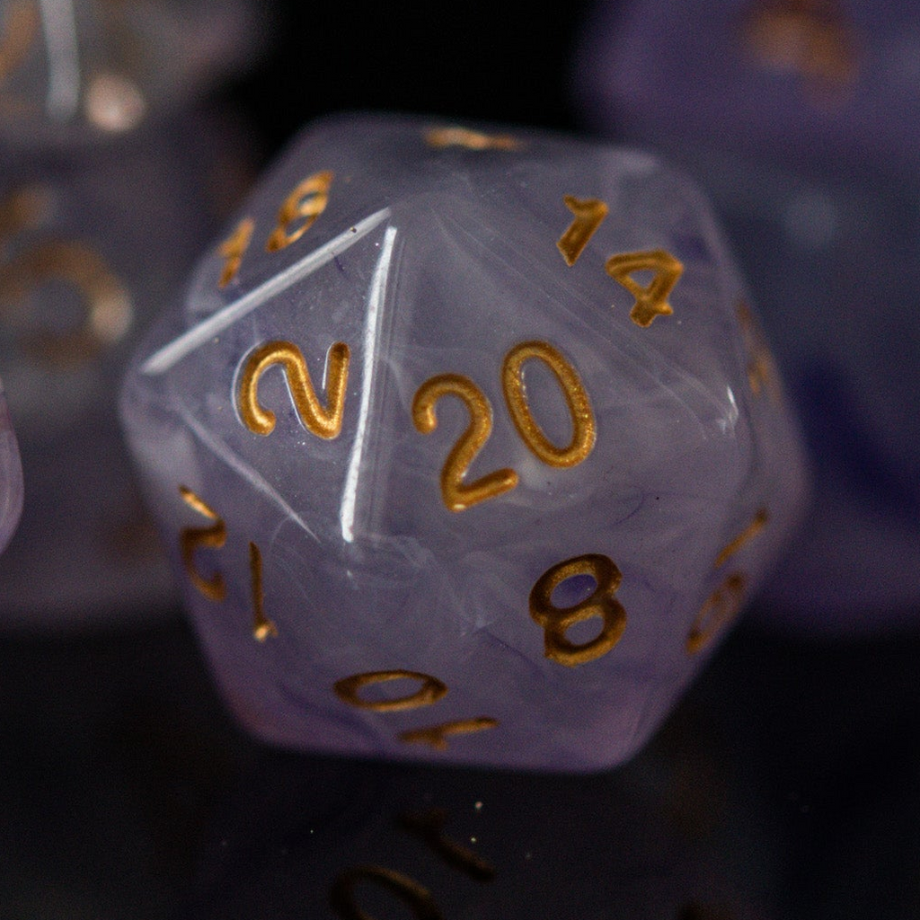 A set of creamy purple acrylic dice with golden engraved numbers, displayed on a reflective surface.