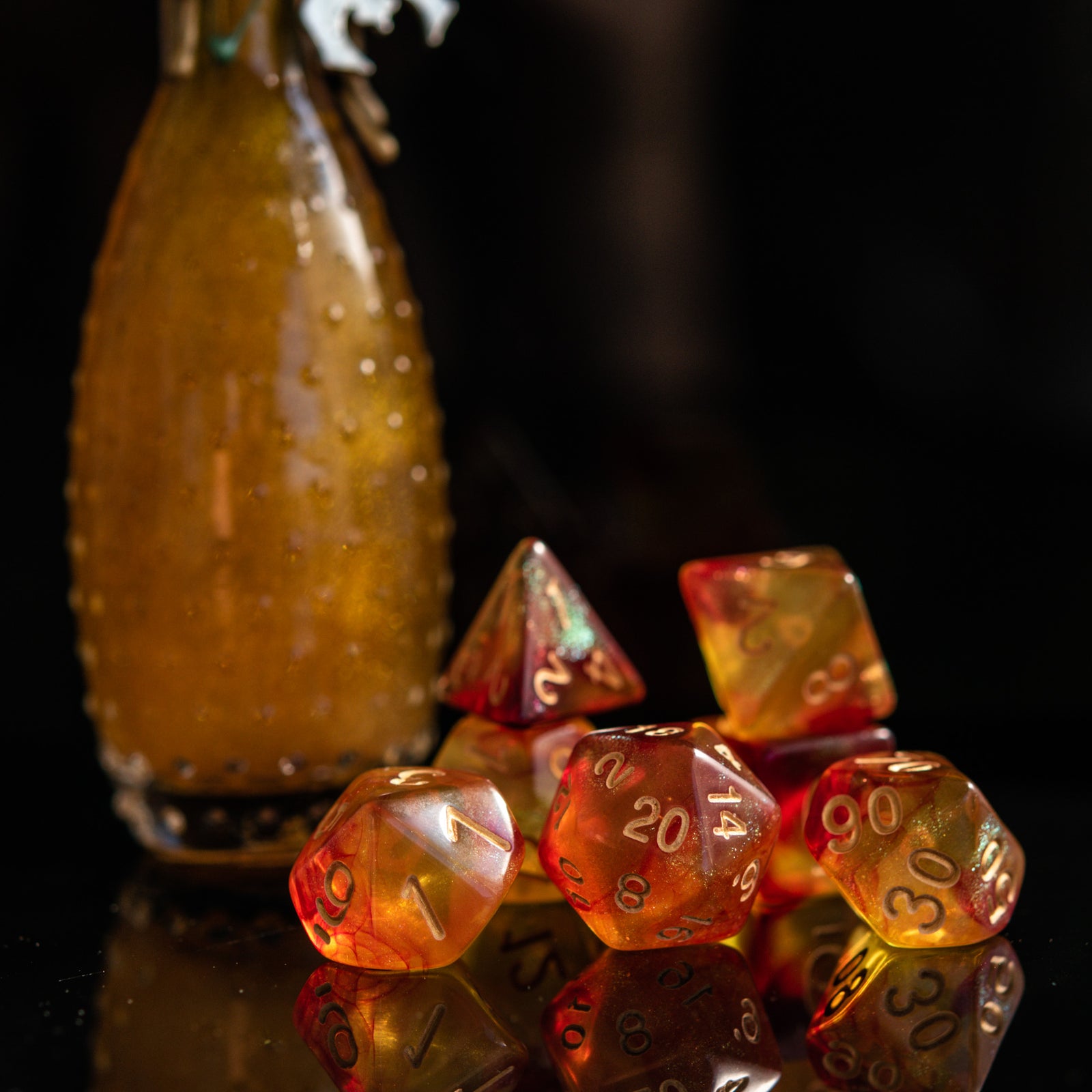 A set of shimmering orange acrylic dice with engraved gold numbers, displayed next to a bottle-shaped container 