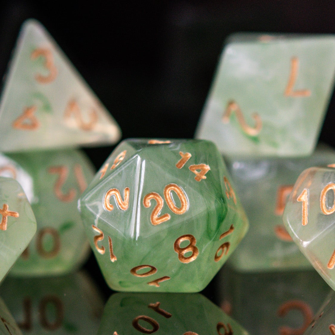 A set of translucent green acrylic dice with engraved numbers, displayed on a reflective surface.
