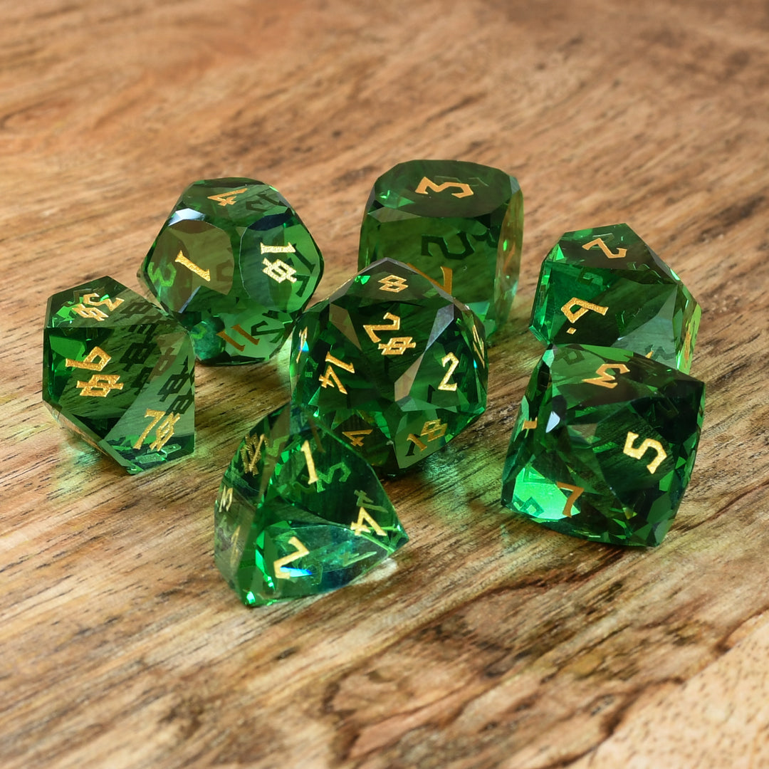 A set of green multifaceted glass dice with engraved numbers, displayed on a wooden surface.