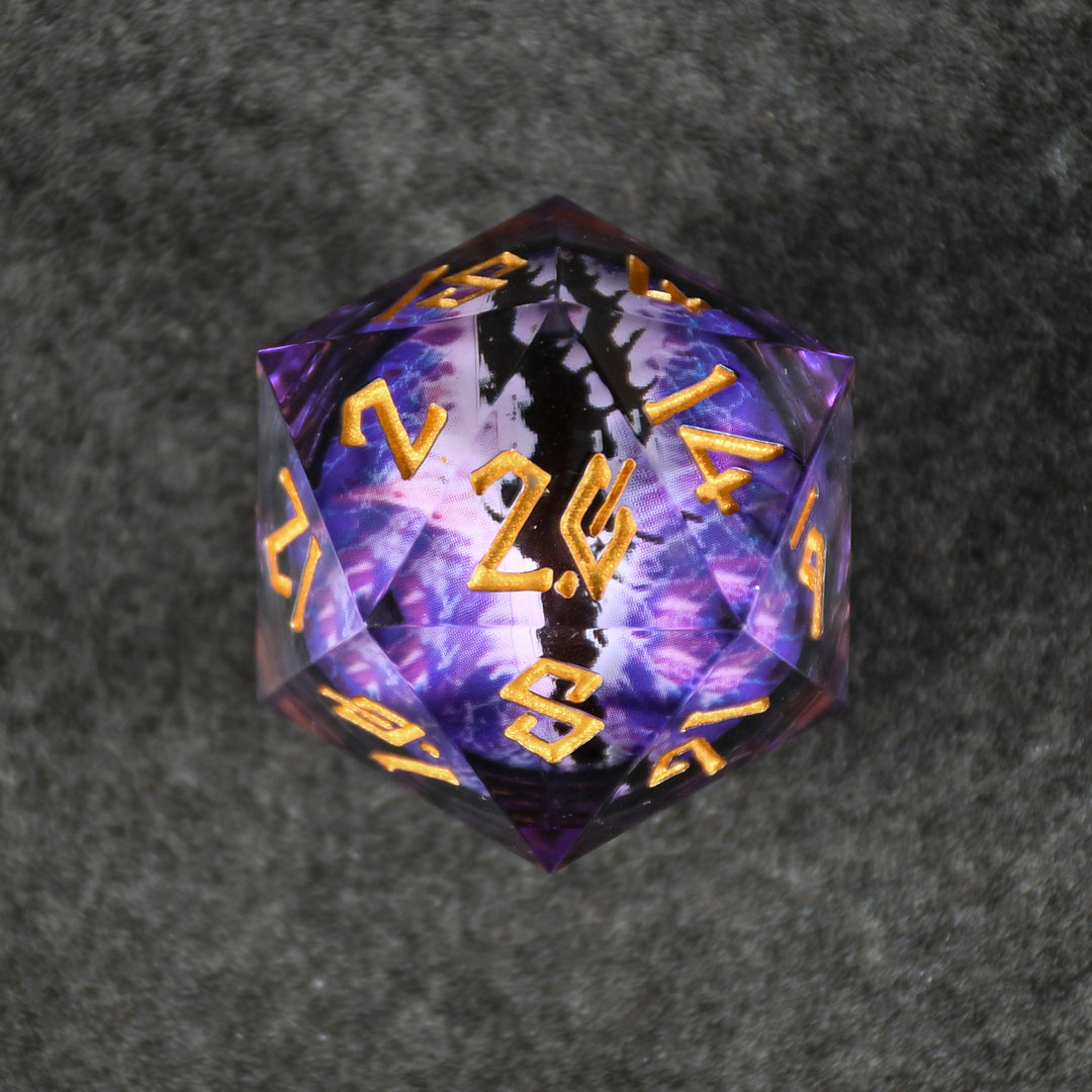 A 30mm clear oversized liquid core d20 dice with gold engraved numbers, featuring a floating purple dragons eye inside. 