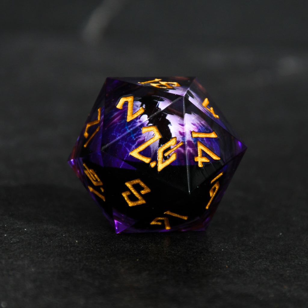 A 30mm clear oversized liquid core d20 dice with gold engraved numbers, featuring a floating purple dragons eye inside. 