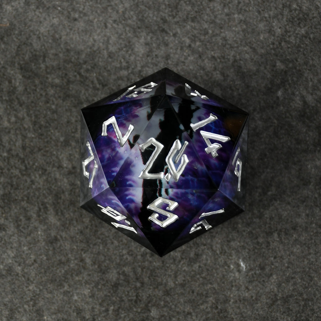 A purple and gold colored, resin-cast, 50mm D20 dice with engraved numbers, appearing to have a floating eyeball in the center, placed on a textured surface.