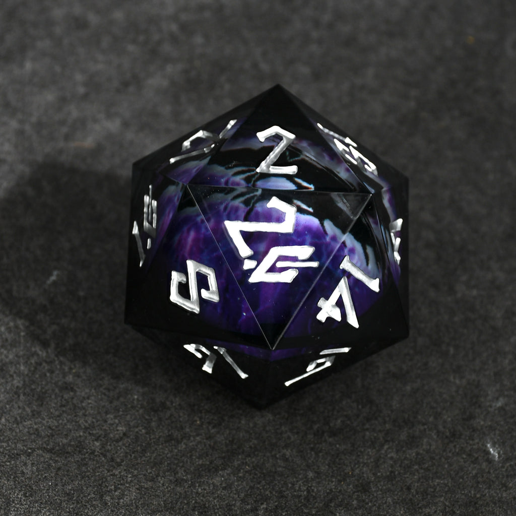A purple and gold colored, resin-cast, 50mm D20 dice with engraved numbers, appearing to have a floating eyeball in the center, placed on a textured surface.