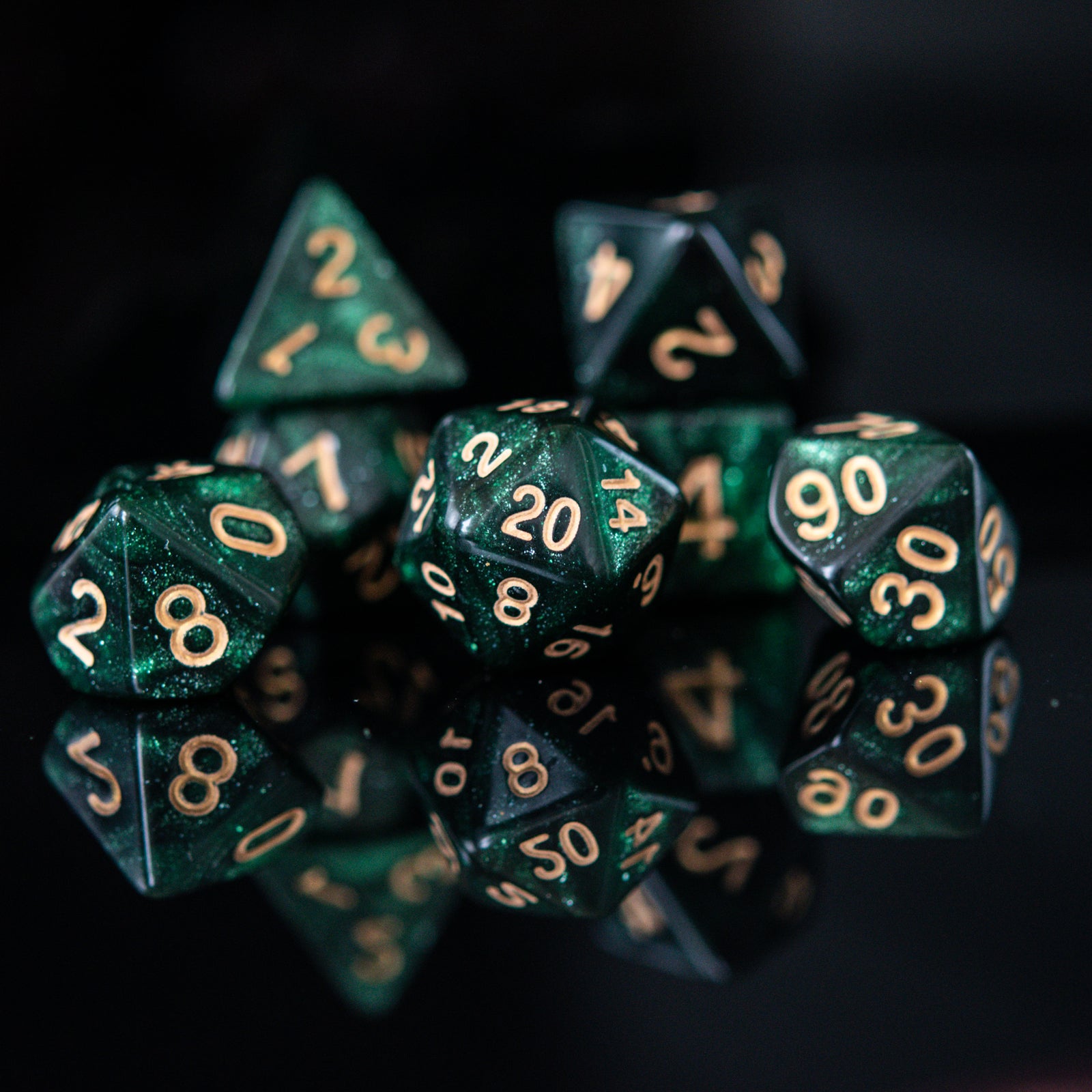 A set of shimmering deep green acrylic dice with engraved gold numbers, displayed on a reflective surface.