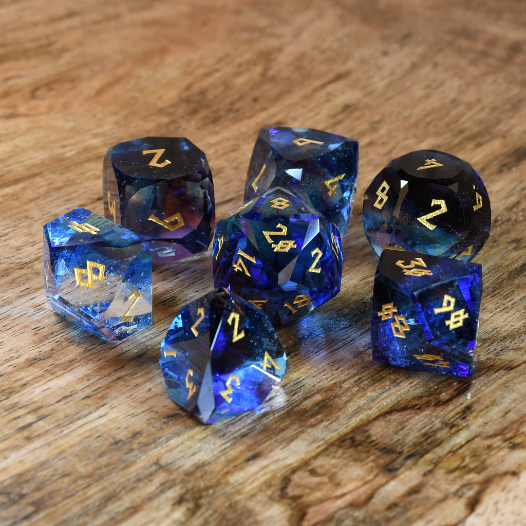 A set of multifaceted blue glass dice with engraved numbers, displayed on a wooden surface.