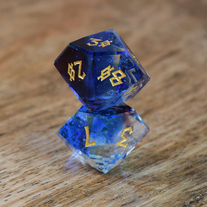 A set of multifaceted blue glass dice with engraved numbers, displayed on a wooden surface.