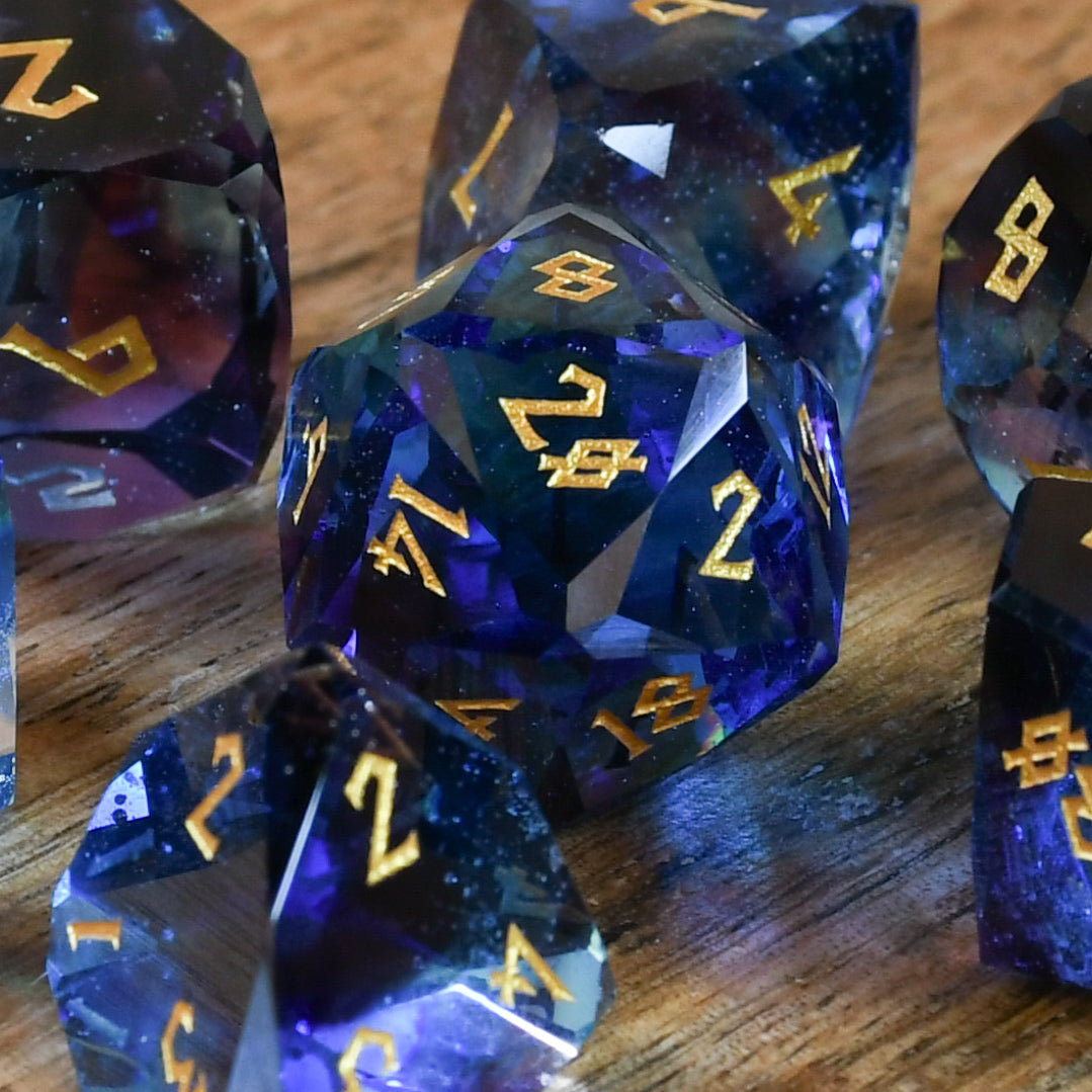 A set of multifaceted blue glass dice with engraved numbers, displayed on a wooden surface.