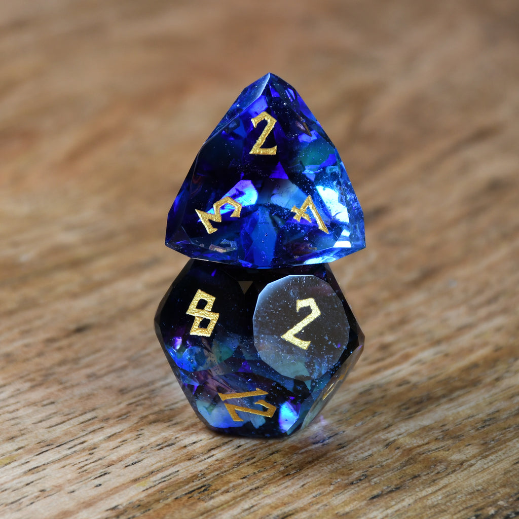 A set of multifaceted blue glass dice with engraved numbers, displayed on a wooden surface.