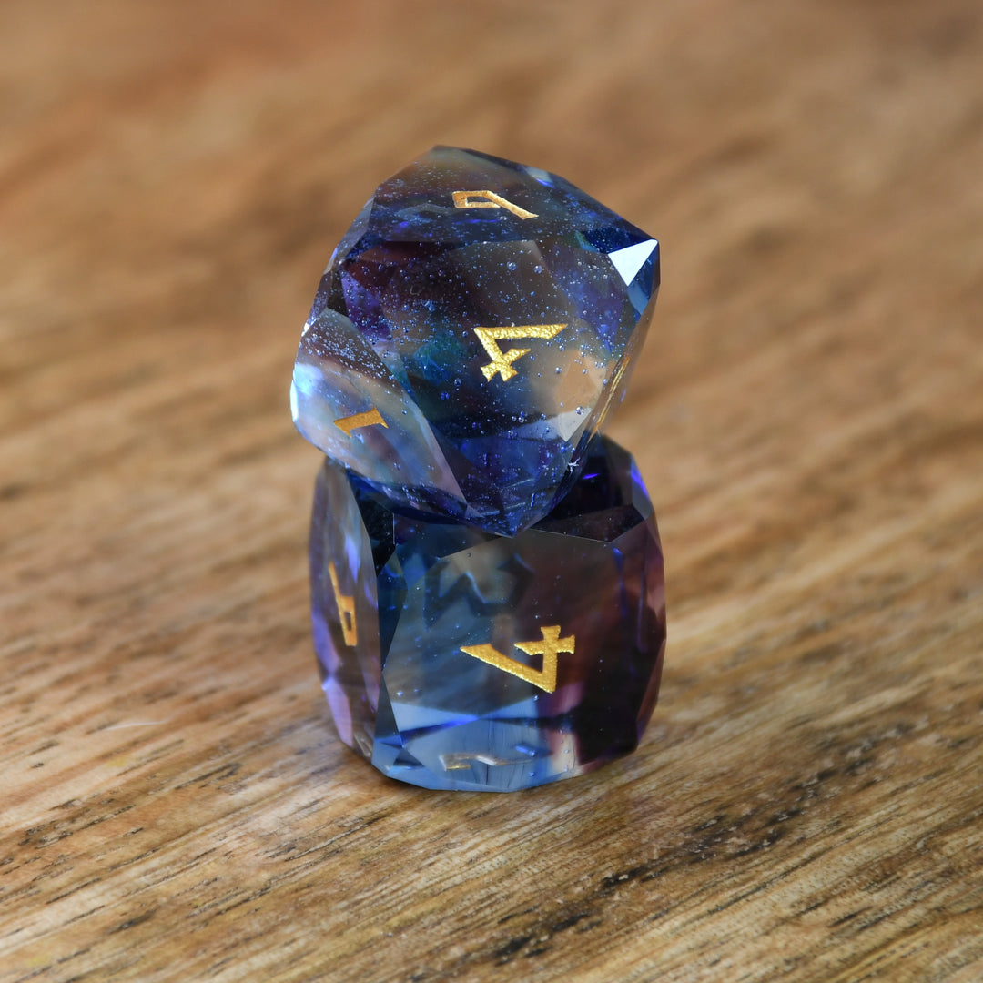 A set of multifaceted blue glass dice with engraved numbers, displayed on a wooden surface.