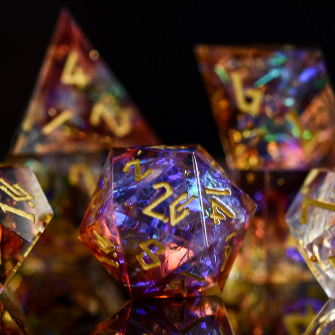 A set of sharp-edged resin dice with engraved numbers, featuring a translucent appearance with gold, orange, and purple colors.