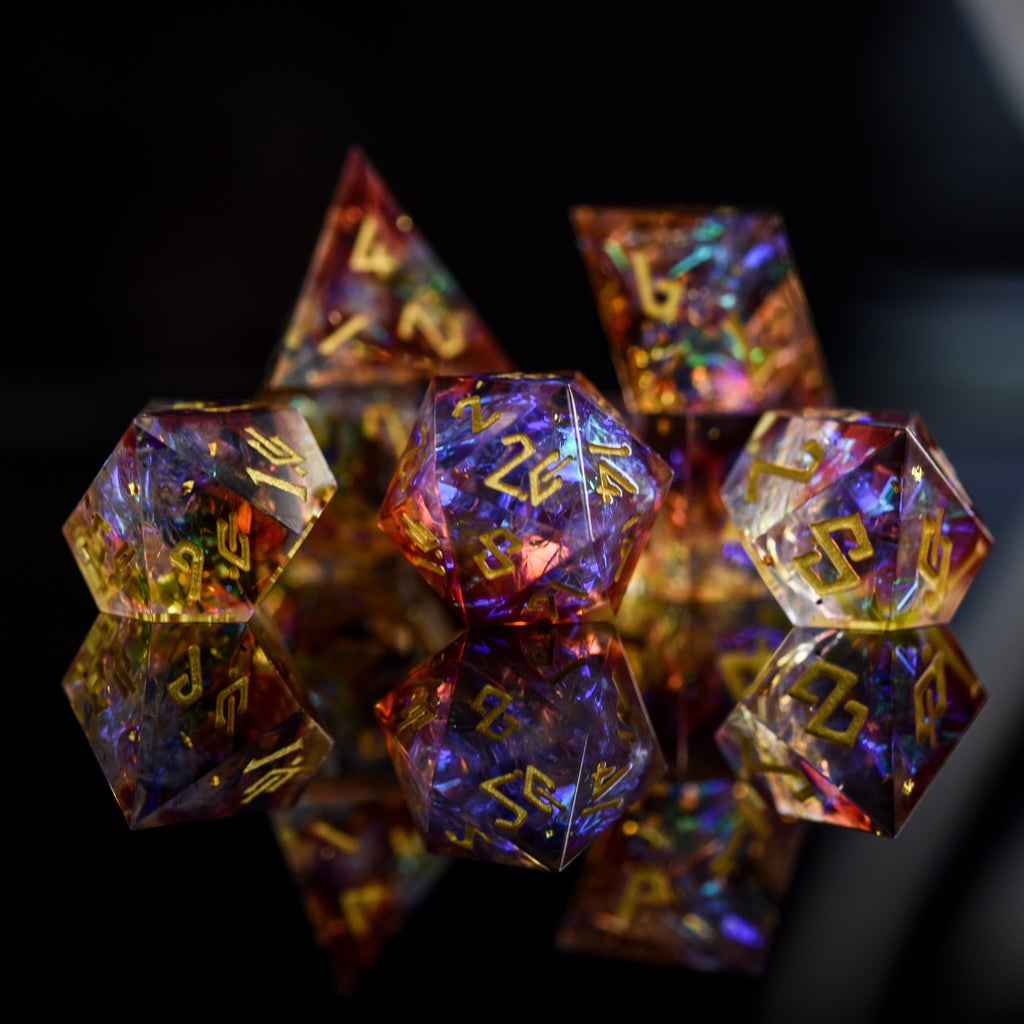 A set of sharp-edged resin dice with engraved numbers, featuring a translucent appearance with gold, orange, and purple colors.