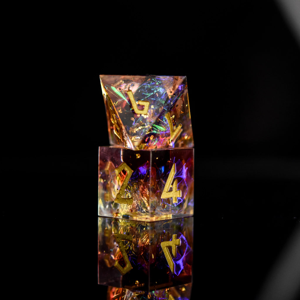 A set of sharp-edged resin dice with engraved numbers, featuring a translucent appearance with gold, orange, and purple colors.