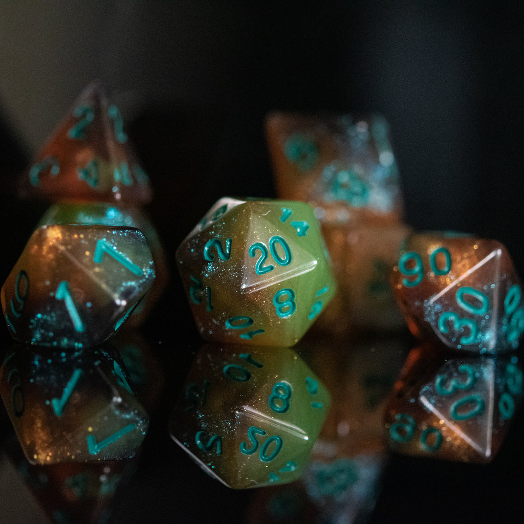A set of acrylic dice with engraved numbers, featuring green and orange color accents, displayed on a reflective surface.