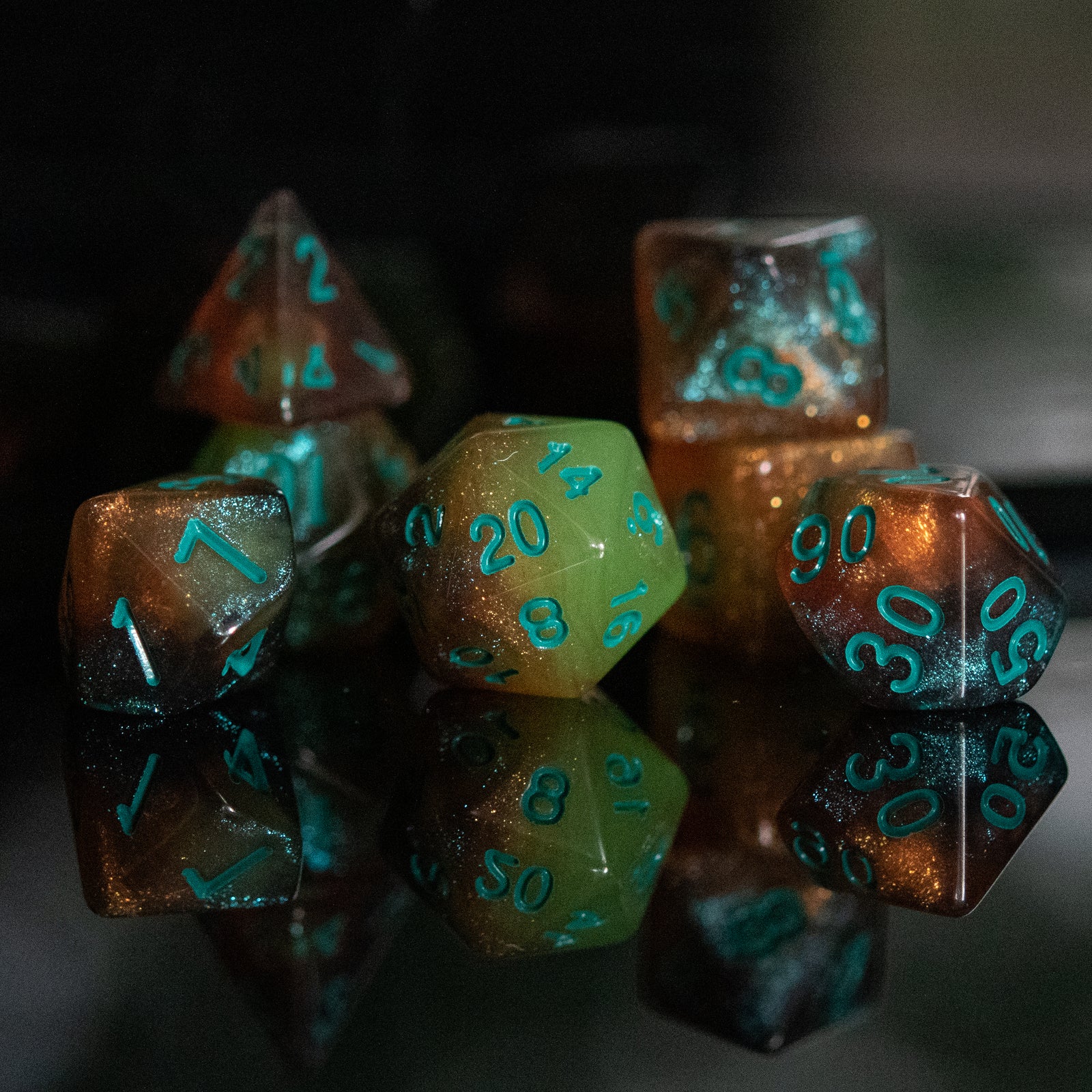 A set of acrylic dice with engraved numbers, featuring green and orange color accents, displayed on a reflective surface.
