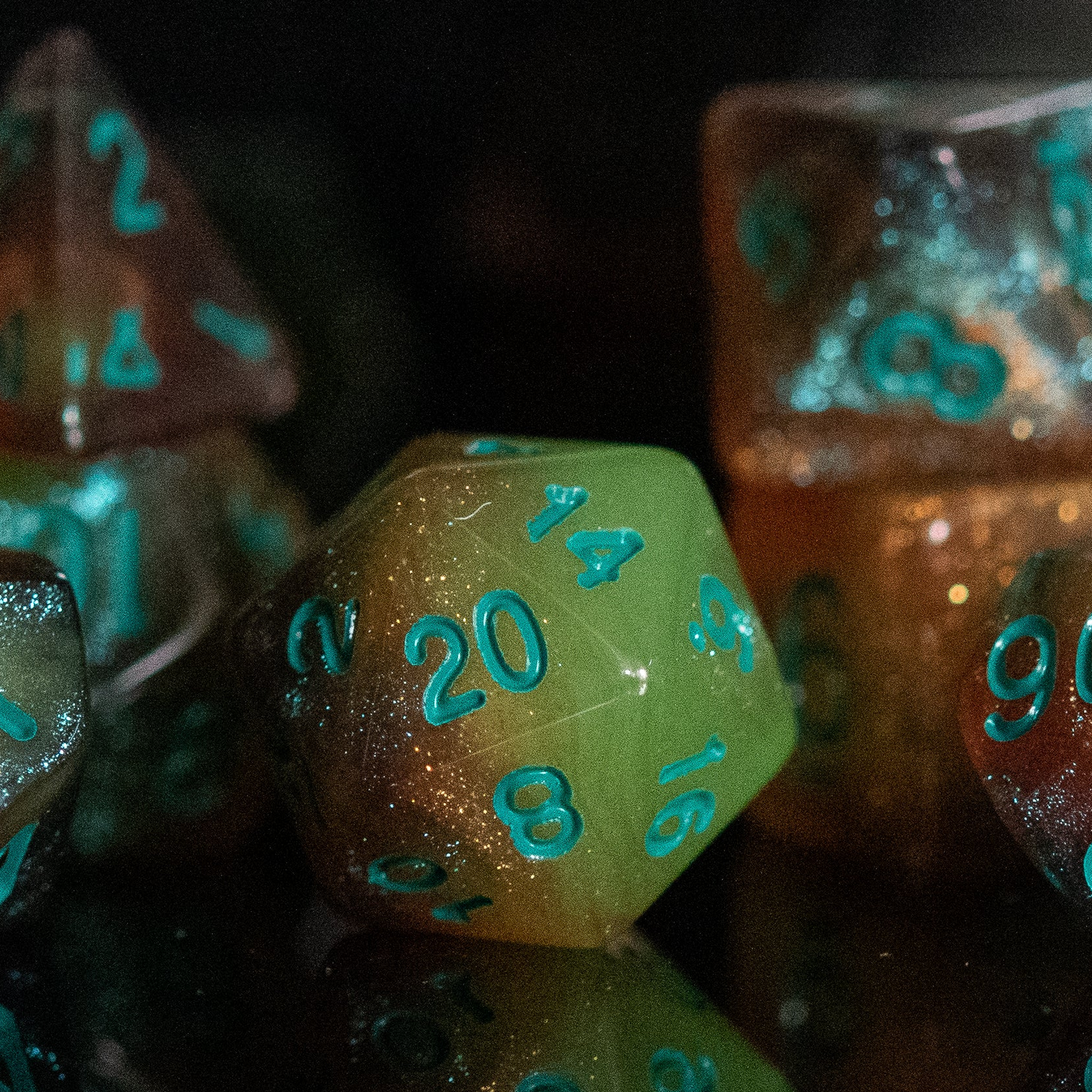 A set of acrylic dice with engraved numbers, featuring green and orange color accents, displayed on a reflective surface.