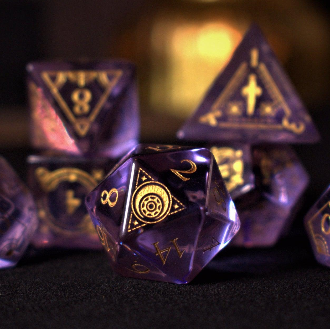 A set of purple glass dice with engraved golden numbers and detail, displayed on a dark surface with a light source in the background creating a reflective sheen on the dice.