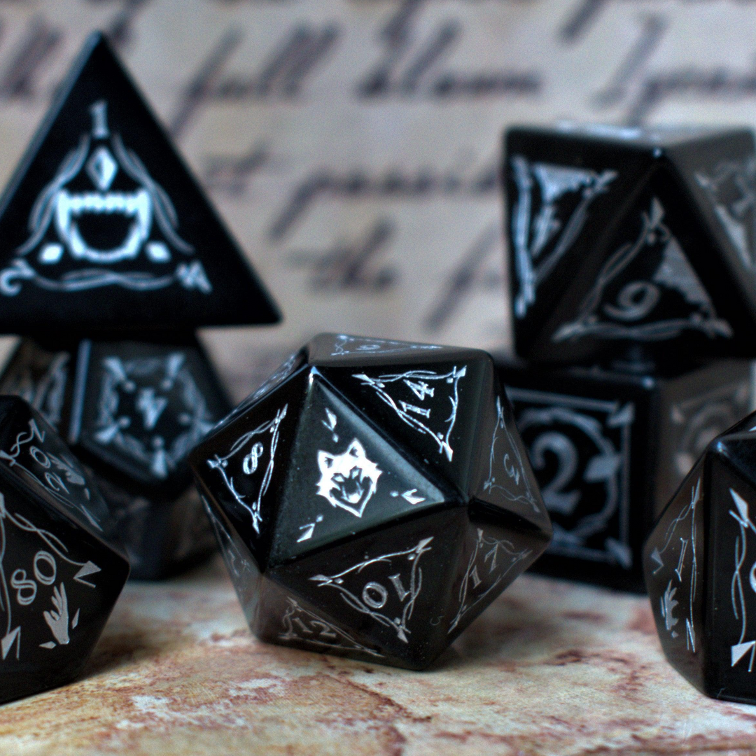 A set of black obsidian stone dnd ttrpg dice with engraved numbers, displayed on a textured surface with a blurred background featuring written text.