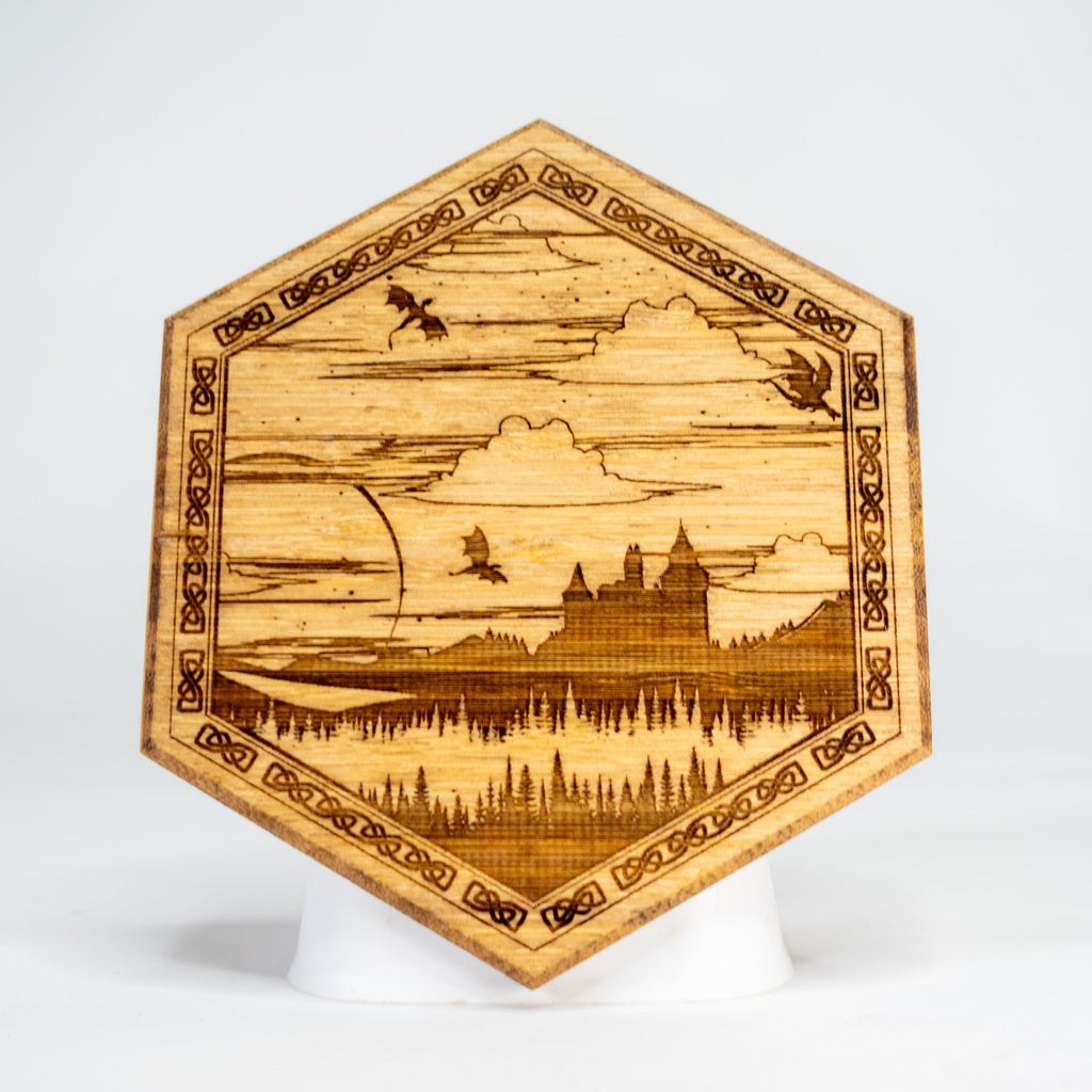 A hexagonal-shaped wooden art puck with intricate fantasy landscape design, including castles and a dragon.