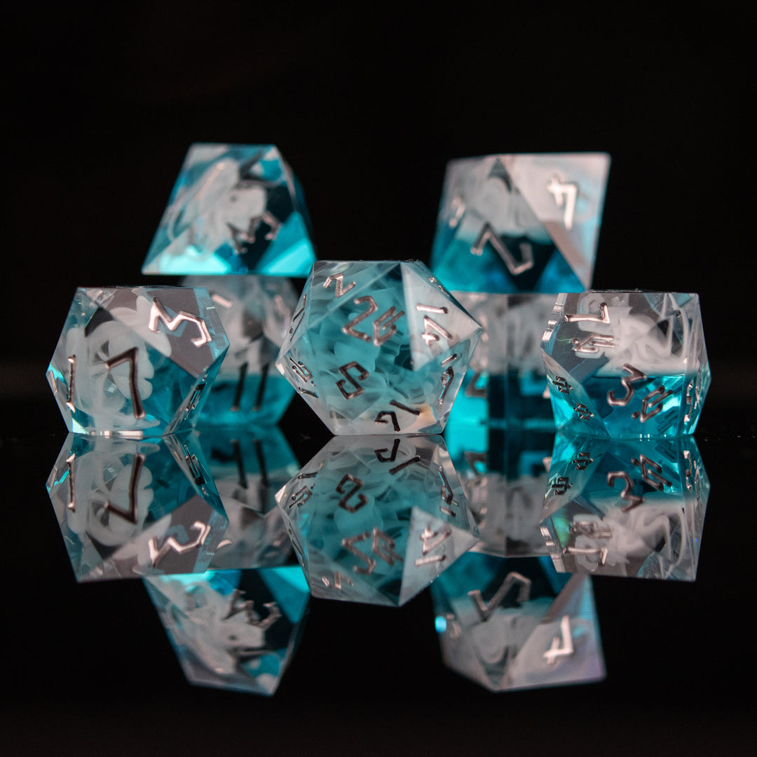 A collection of sharp-edged, blue and white resin dice with silver engraved numbers, reflecting on a black surface.