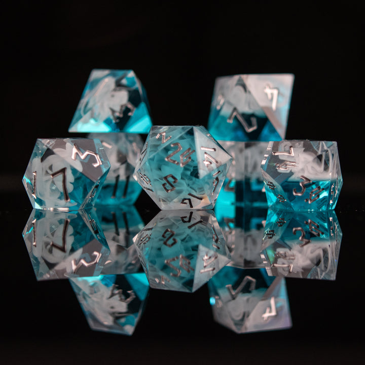 A collection of sharp-edged, blue and white resin dice with silver engraved numbers, reflecting on a black surface.