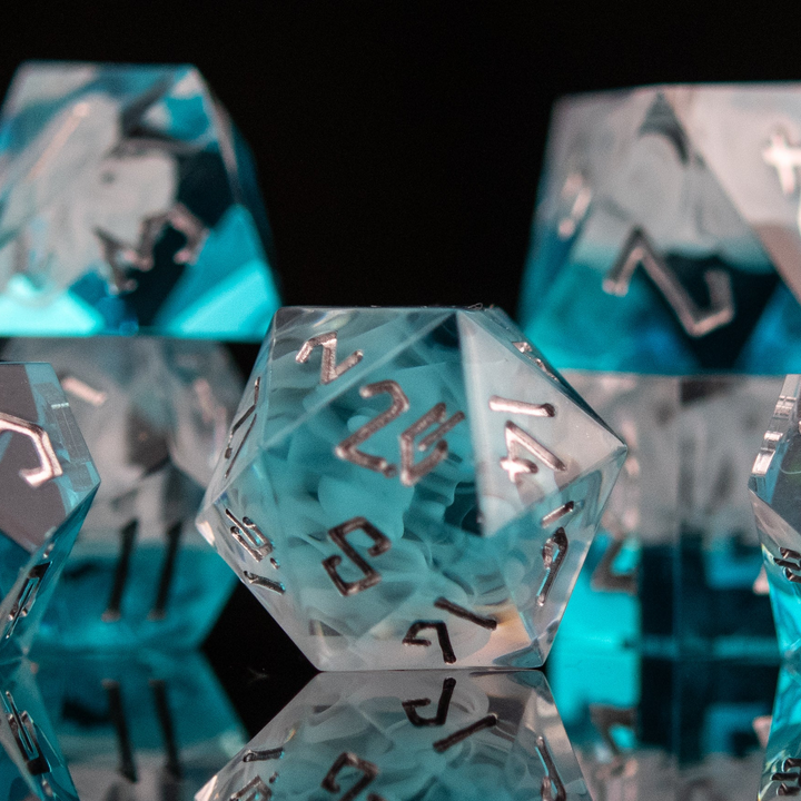 A collection of sharp-edged, blue and white resin dice with silver engraved numbers, reflecting on a black surface.