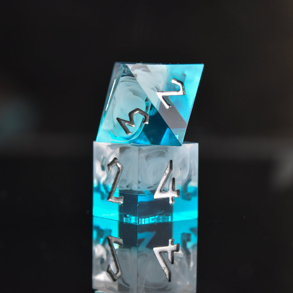 A collection of sharp-edged, blue and white resin dice with silver engraved numbers, reflecting on a black surface.