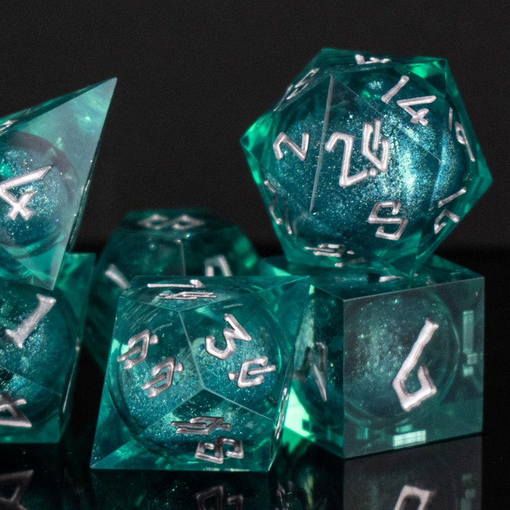 A set of teal resin dice with silver hand-painted numbers, including various shapes such as a d4, d6, d8, d10, d12, and d20, displayed on a reflective surface.