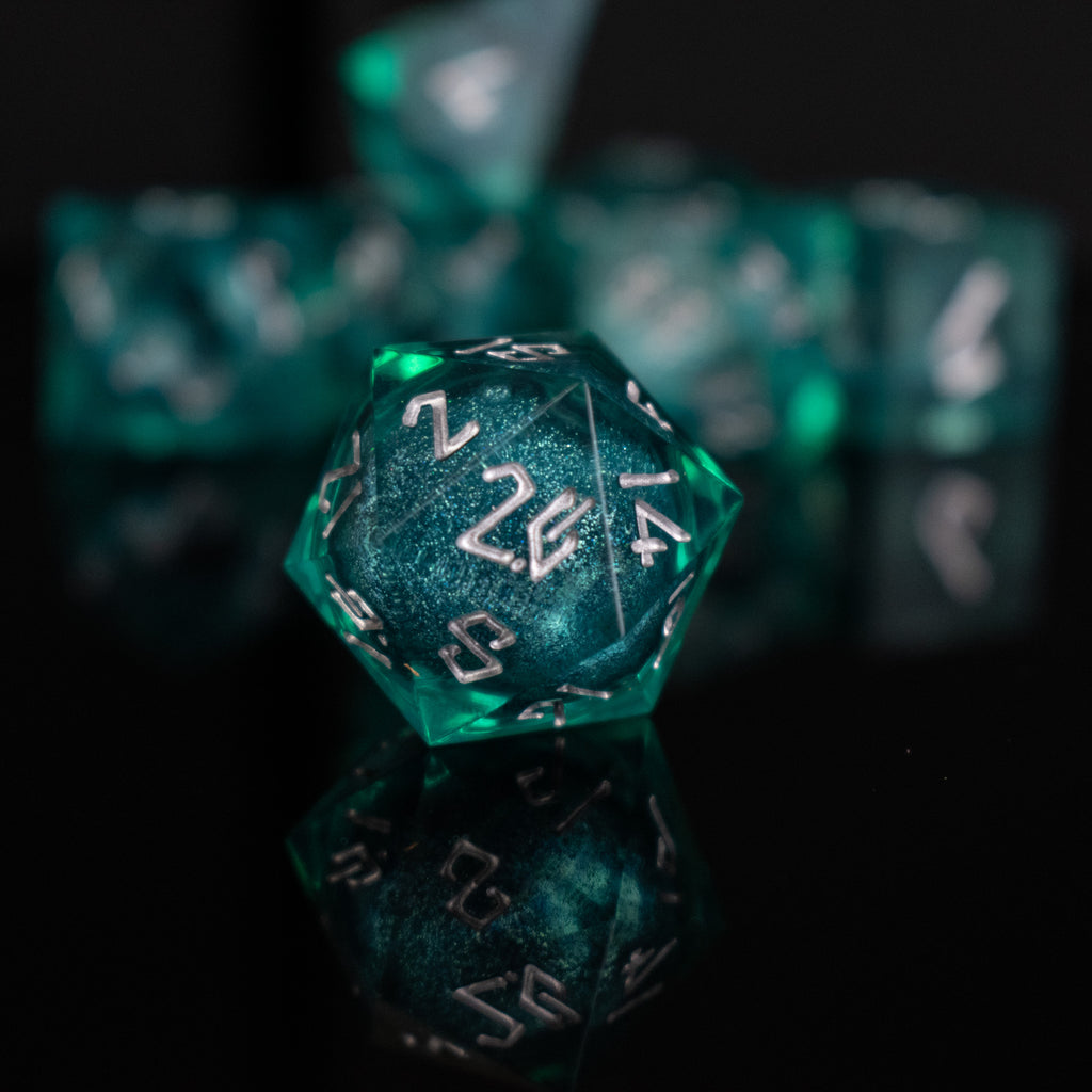 A set of teal resin dice with silver hand-painted numbers, including various shapes such as a d4, d6, d8, d10, d12, and d20, displayed on a reflective surface.