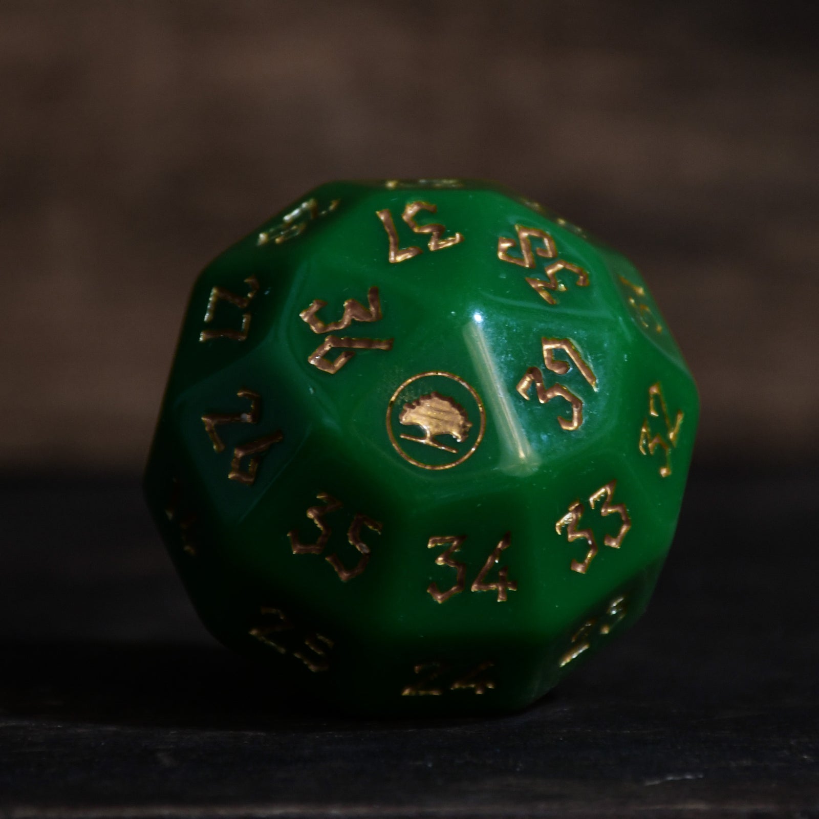 A green acrylic dice with engraved numbers and a symbol on one face, placed on a wooden surface.