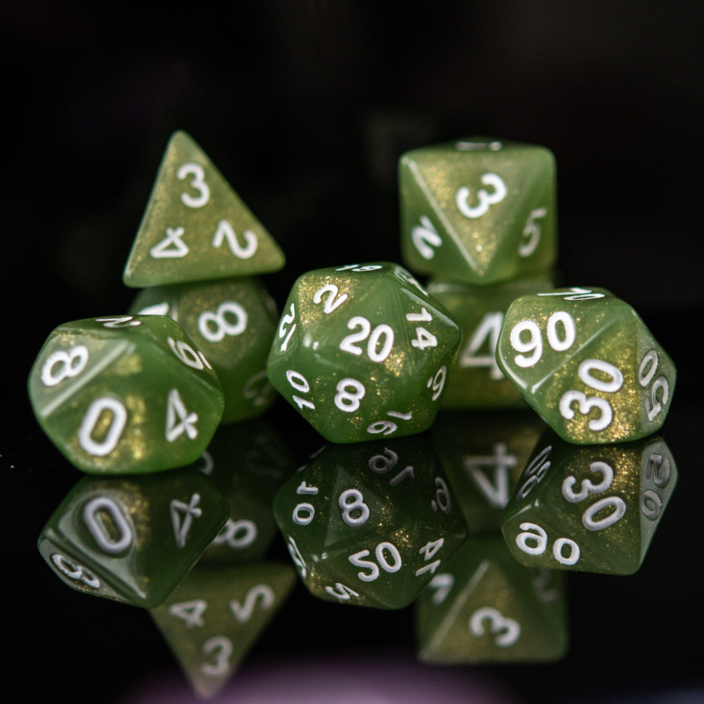 A set of green glittery acrylic dice with white numbering, displayed in front of a translucent container with a lid, against a dark background.