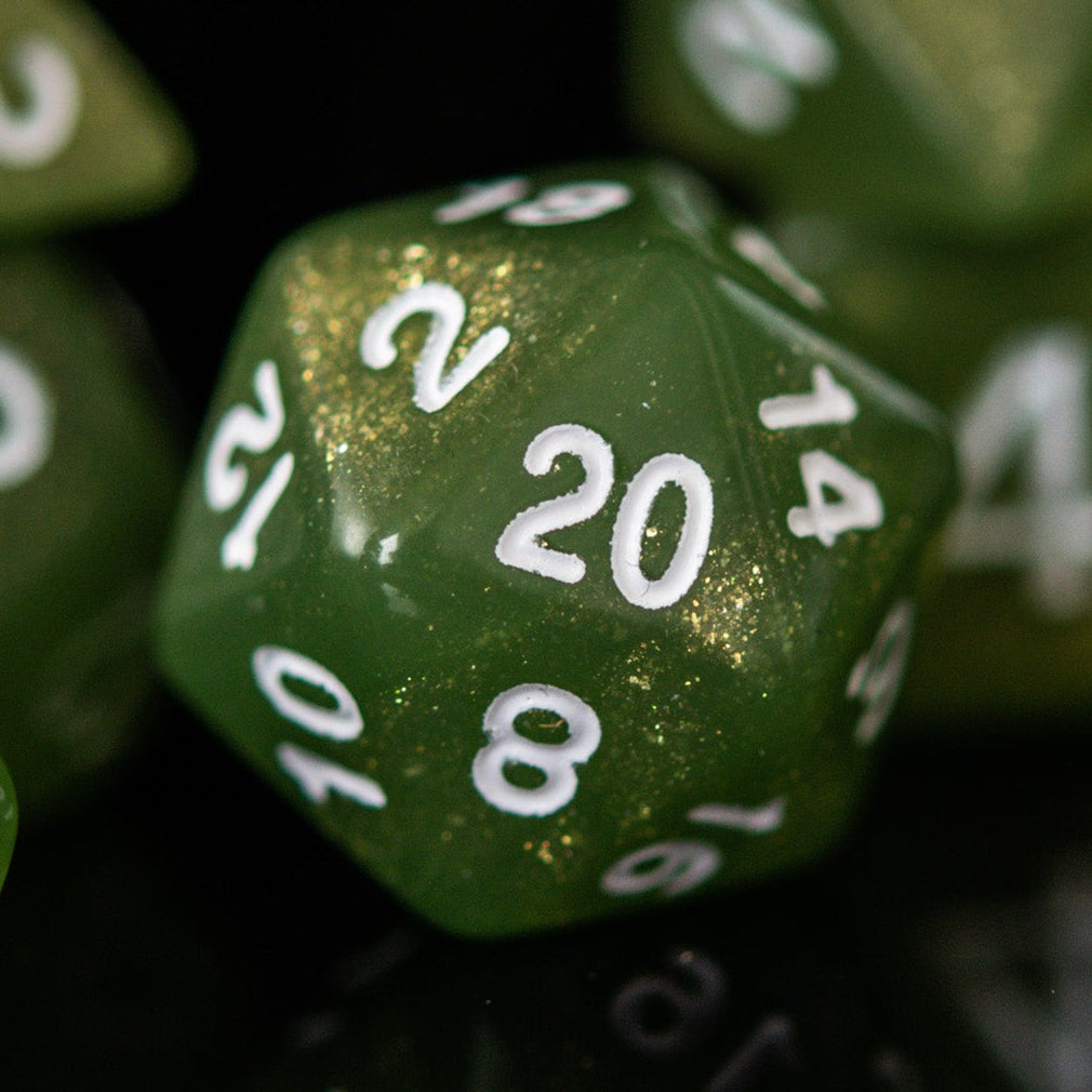 A set of green glittery acrylic dice with white numbering, displayed in front of a translucent container with a lid, against a dark background.