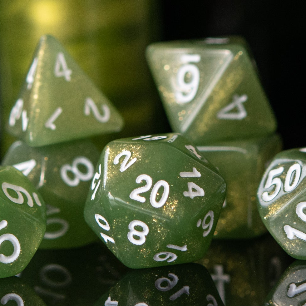A set of green glittery acrylic dice with white numbering, displayed in front of a translucent container with a lid, against a dark background.