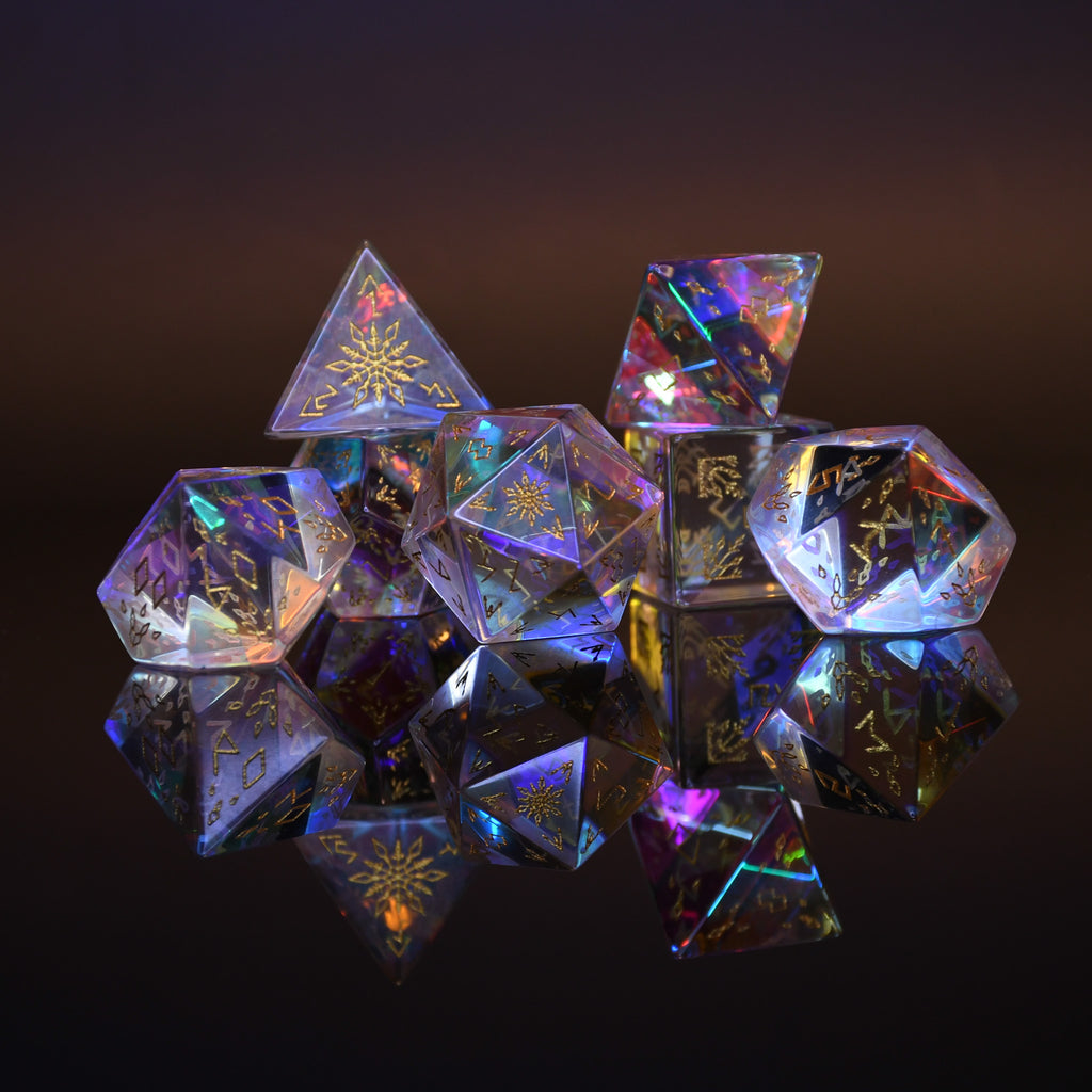 A set of hand-carved, multicolored prismatic glass dice with engraved golden numbering and details, polished and displayed on a reflective surface.