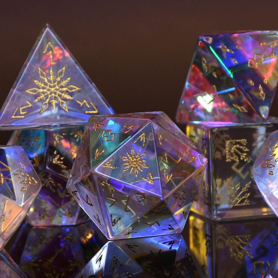 A set of hand-carved, multicolored prismatic glass dice with engraved golden numbering and details, polished and displayed on a reflective surface.