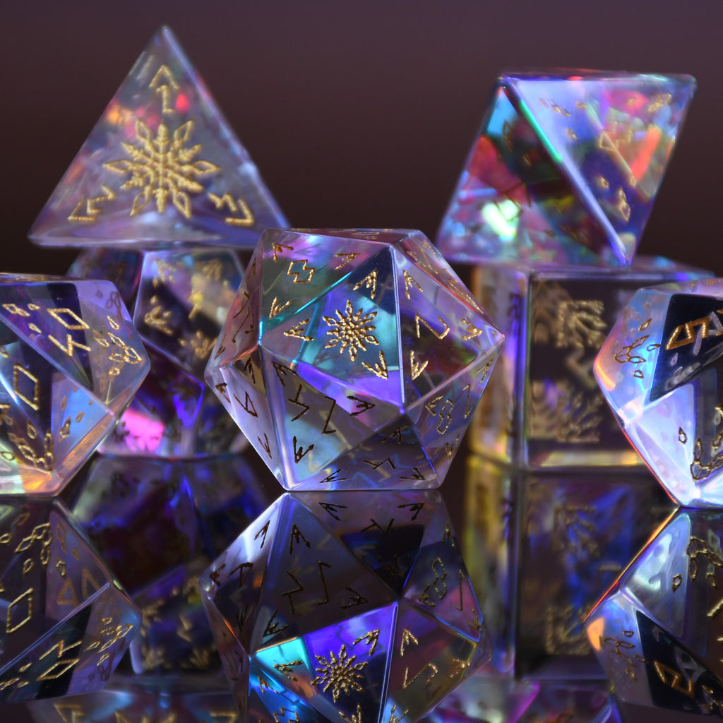 A set of hand-carved, multicolored prismatic glass dice with engraved golden numbering and details, polished and displayed on a reflective surface.