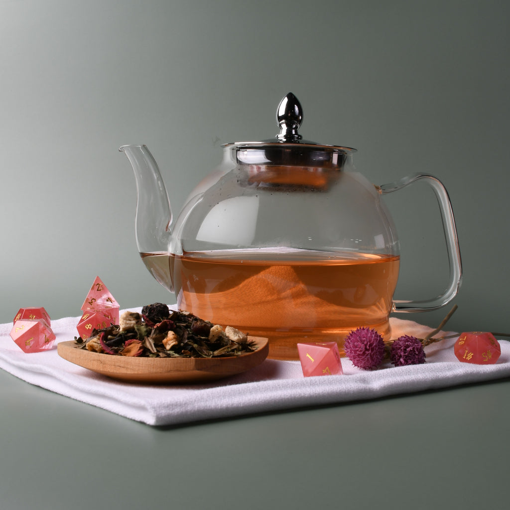 Stone quartz dnd dice beside a wooden plate of misty mountain gaming loose tea leaves and a glass tea pot