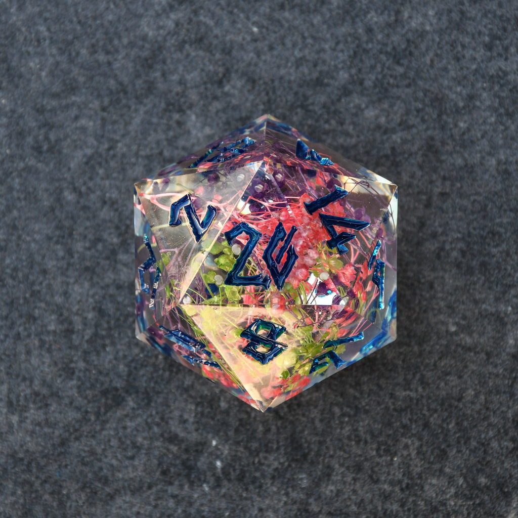 A hand-crafted blue and multicolor resin dice with hand-painted numbers, a 30mm D20, on a dark background.