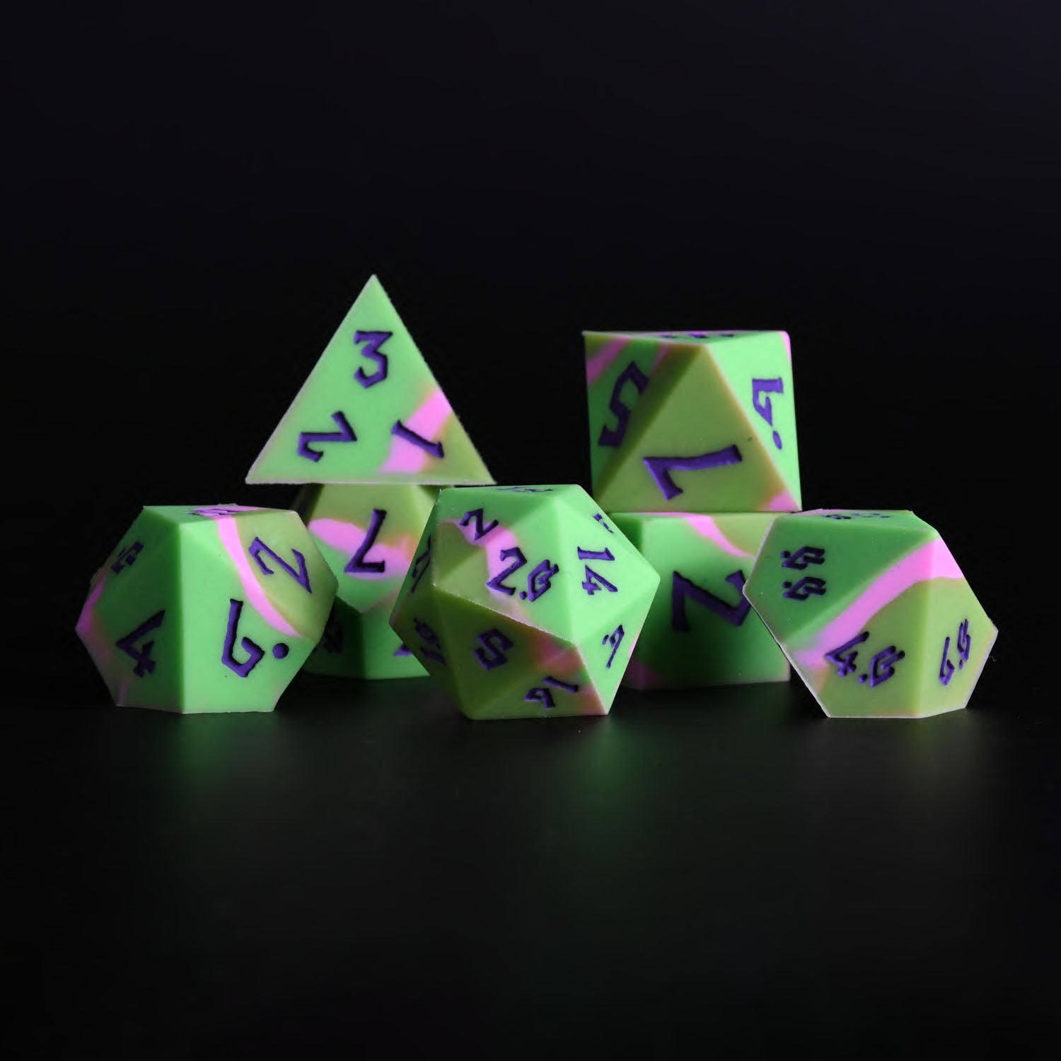 A set of silicone dice in various shapes including a D4, D6, D8, D10, D12, and D20, with green coloring and purple numbers. The dice are displayed against a dark background.