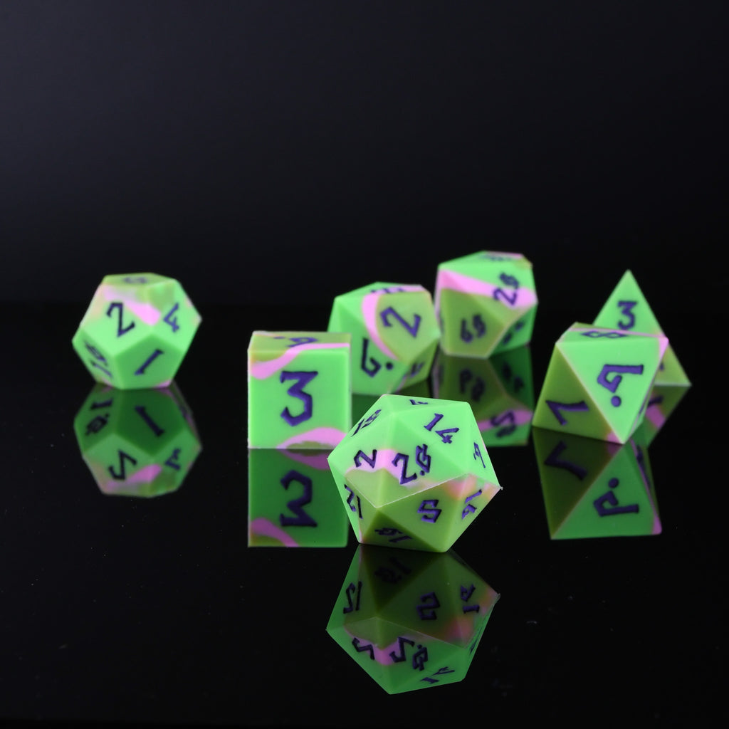 A set of silicone dice in various shapes including a D4, D6, D8, D10, D12, and D20, with green coloring and purple numbers. The dice are displayed against a dark background.