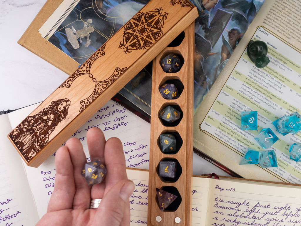 Wooden dice holder with engraved design on a surface with books and papers.
