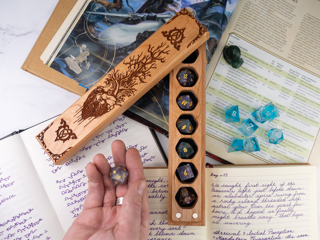 Wooden dice holder with engraved design on a surface with books and dice.